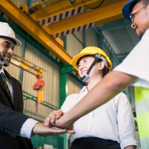 Concept of teamwork in Factory. Working team stack or gather hands together of smiling businessman, techician with safety hardhat helmet. Synergy and happyiness concept